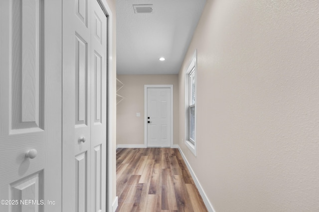 corridor featuring wood finished floors, visible vents, and baseboards