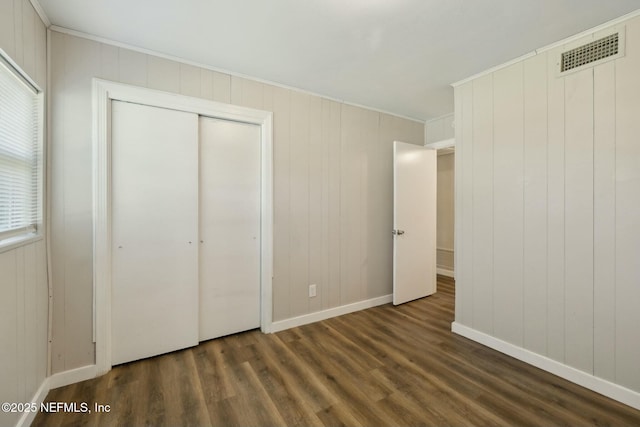 unfurnished bedroom with dark wood-style floors, visible vents, baseboards, and ornamental molding