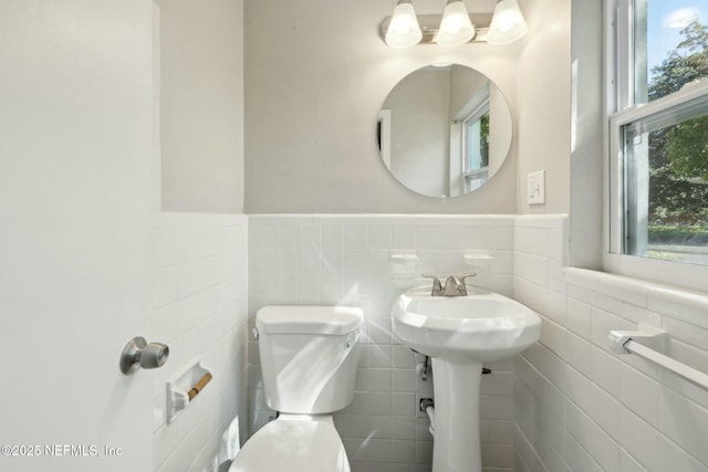 half bathroom featuring wainscoting, toilet, and tile walls