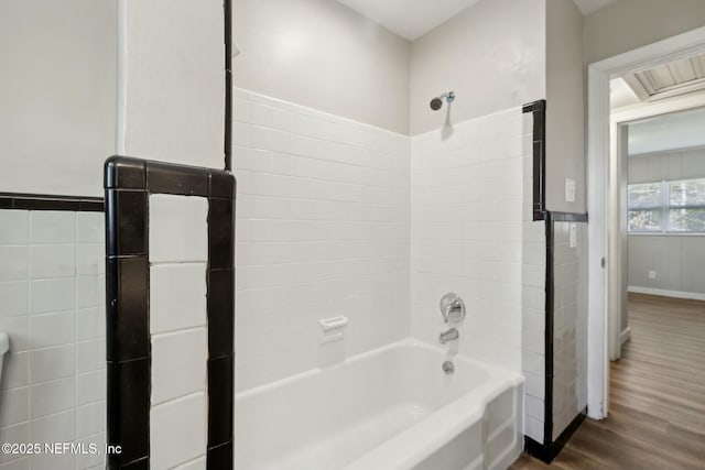 bathroom with wainscoting, wood finished floors, shower / bathing tub combination, and tile walls