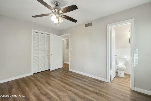 unfurnished bedroom with baseboards, ensuite bath, visible vents, a closet, and wood finished floors