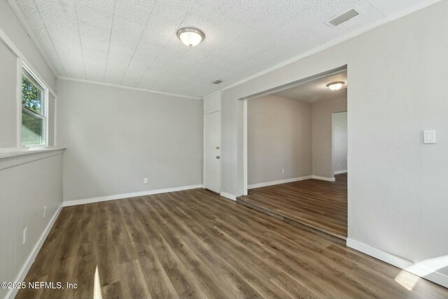 empty room with baseboards, visible vents, crown molding, and wood finished floors