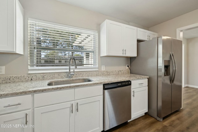 kitchen featuring stainless steel appliances, dark wood finished floors, a sink, light stone counters, and white cabinets