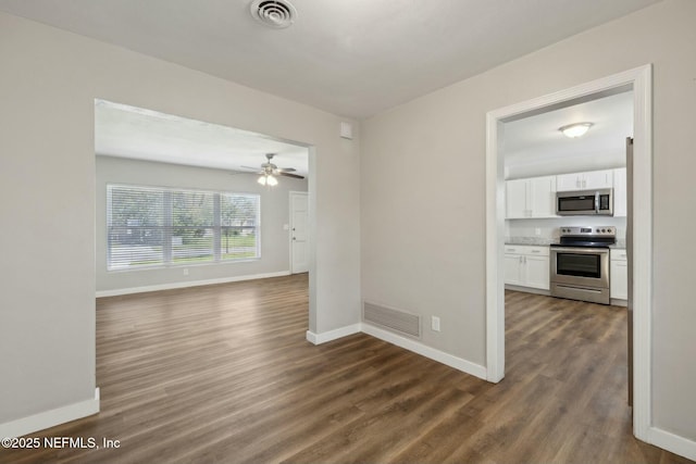empty room featuring a ceiling fan, dark wood finished floors, baseboards, and visible vents