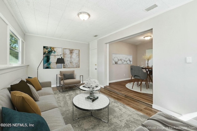 living area featuring wood finished floors, crown molding, baseboards, and visible vents