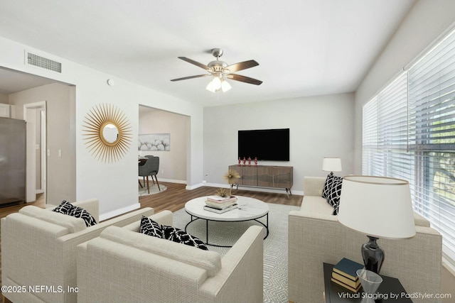 living room featuring baseboards, visible vents, a ceiling fan, and wood finished floors
