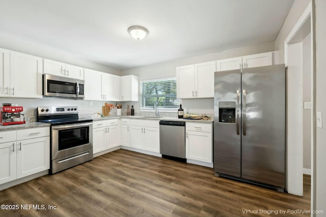 kitchen featuring light stone countertops, stainless steel appliances, white cabinetry, a sink, and dark wood-style floors