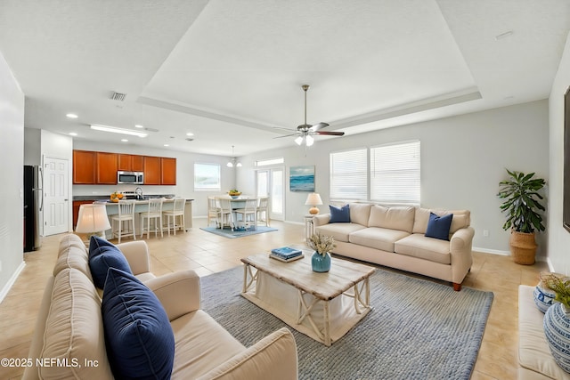 living area featuring light tile patterned floors, a tray ceiling, visible vents, and a wealth of natural light