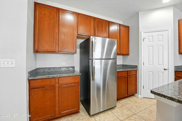 kitchen with dark stone counters, light tile patterned flooring, freestanding refrigerator, and a textured ceiling