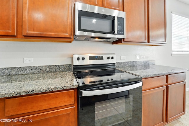 kitchen featuring light stone counters, electric range, stainless steel microwave, and brown cabinetry