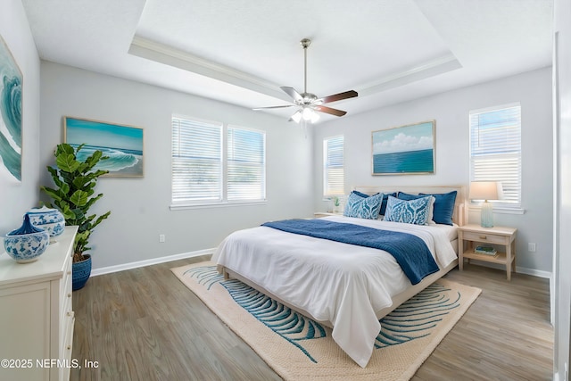 bedroom with a raised ceiling, multiple windows, and light wood finished floors