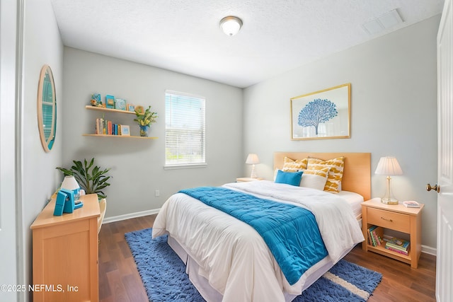 bedroom with visible vents, baseboards, a textured ceiling, and wood finished floors