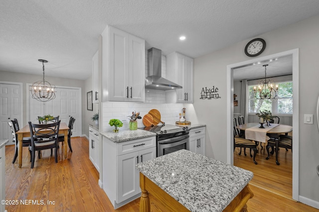 3079 Anderson Rd, Green Cove Springs, FL 32043 - kitchen with stainless steel range with electric cooktop, light wood-style floors, white cabinetry, wall chimney exhaust hood, and a chandelier