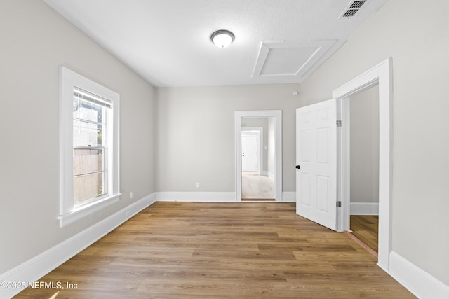 empty room with attic access, visible vents, light wood-type flooring, and baseboards