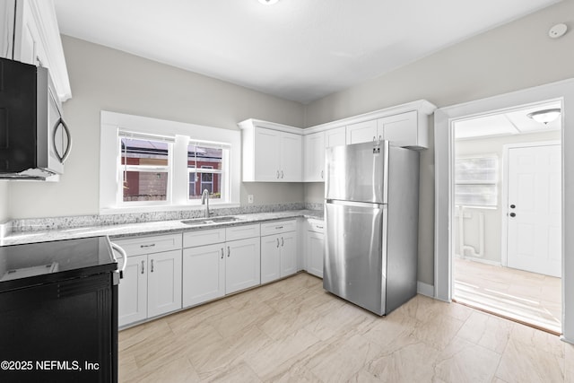 kitchen with a sink, light stone countertops, appliances with stainless steel finishes, and white cabinets