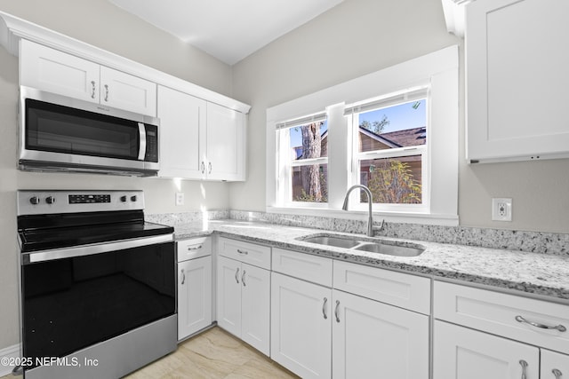 kitchen with light stone counters, white cabinets, appliances with stainless steel finishes, and a sink