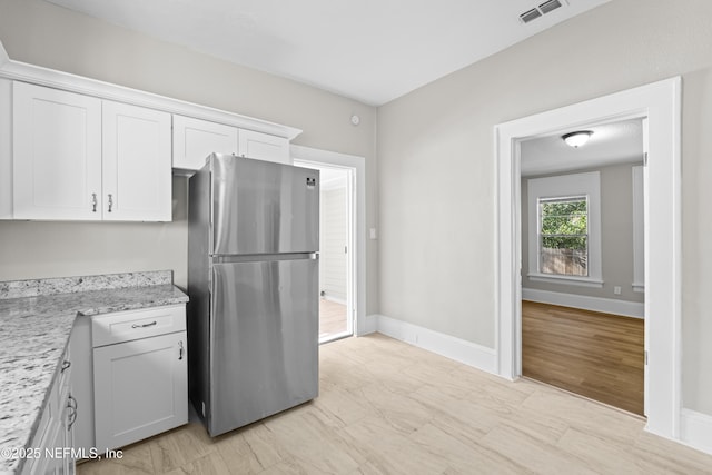 kitchen with visible vents, freestanding refrigerator, baseboards, white cabinets, and light stone countertops