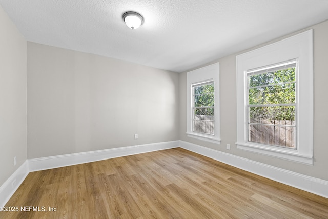 unfurnished room featuring light wood-style flooring, a textured ceiling, and baseboards