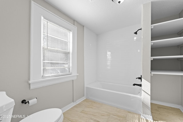 bathroom with a textured ceiling, toilet, shower / bathtub combination, and baseboards