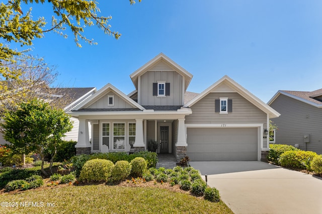 craftsman house featuring stone siding, covered porch, board and batten siding, and driveway