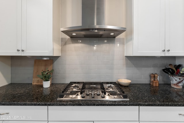 kitchen featuring wall chimney range hood, stainless steel gas stovetop, backsplash, and white cabinetry