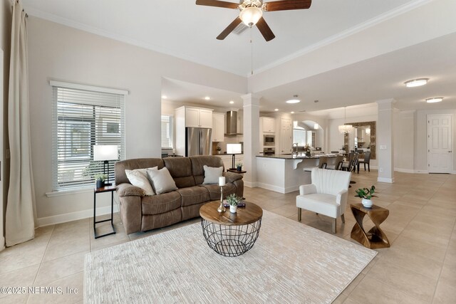 living area with baseboards, crown molding, ceiling fan, and ornate columns