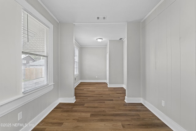 hall with dark wood finished floors, baseboards, visible vents, and ornamental molding