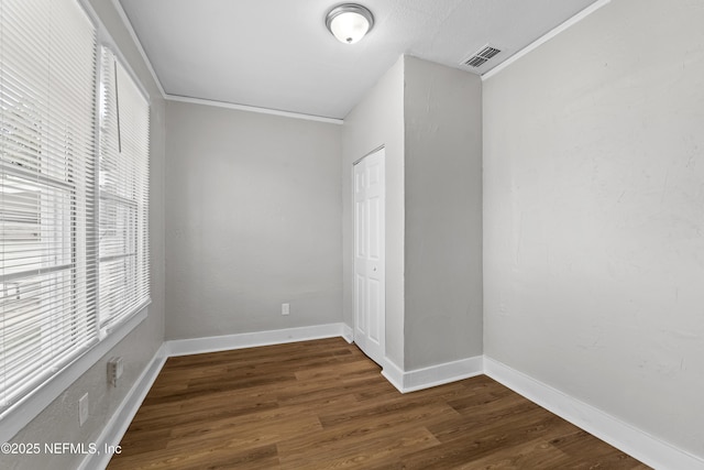unfurnished room featuring crown molding, dark wood-style floors, visible vents, and baseboards