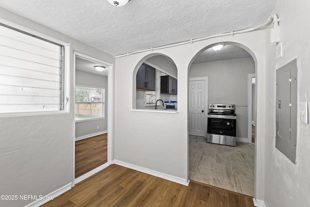hallway featuring arched walkways, a textured ceiling, baseboards, and wood finished floors