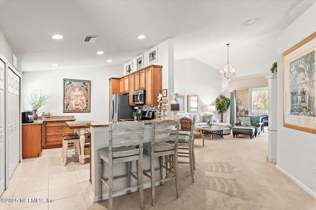 11856 Surfbird Cir Unit 41E, Jacksonville, FL 32256 - kitchen with a breakfast bar, stainless steel appliances, vaulted ceiling, brown cabinetry, and a notable chandelier