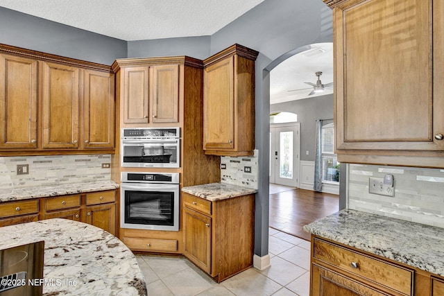 1317 Honeysuckle Dr, Saint Johns, FL 32259 - kitchen with brown cabinetry, decorative backsplash, arched walkways, and ceiling fan