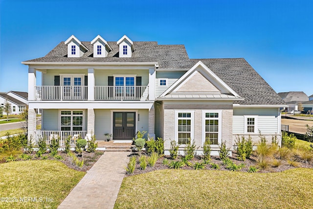 view of front facade with a balcony, covered porch, a front lawn, french doors, and brick siding