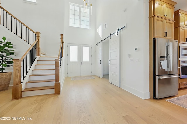 entryway featuring a barn door, light wood-style floors, a high ceiling, baseboards, and stairs