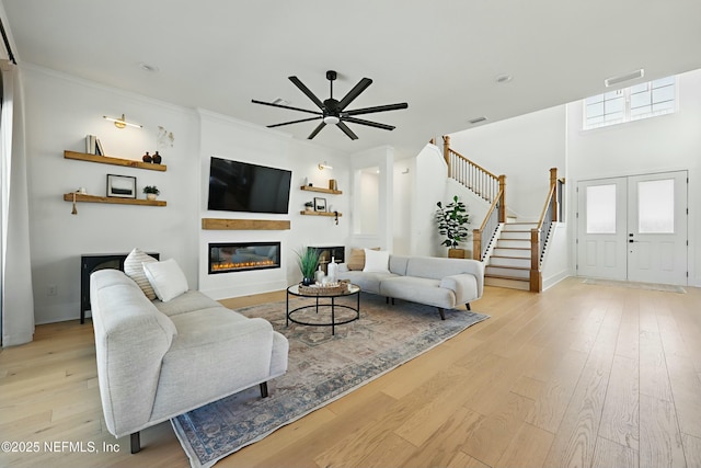 living area featuring visible vents, a ceiling fan, a glass covered fireplace, light wood-style floors, and stairs