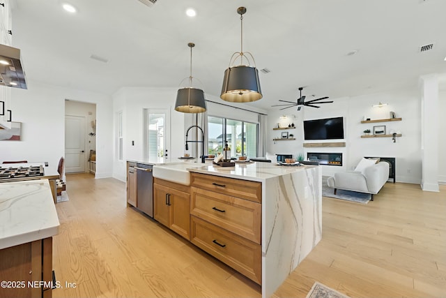 kitchen featuring a sink, stainless steel dishwasher, a glass covered fireplace, light wood-style floors, and ceiling fan