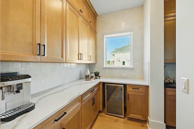 kitchen with light stone counters, light wood-style floors, backsplash, and beverage cooler