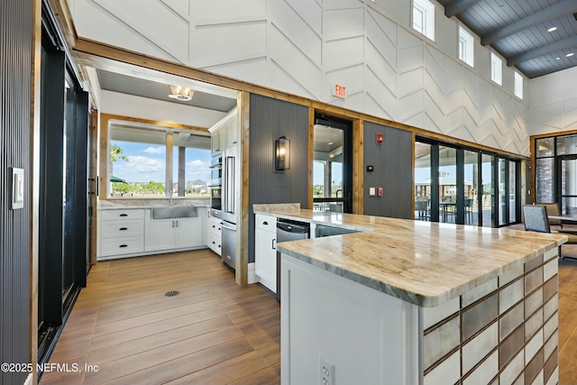 kitchen featuring wood ceiling, light stone counters, a peninsula, white cabinetry, and a sink