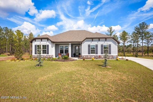 view of front of property with stone siding, concrete driveway, a front lawn, and a shingled roof