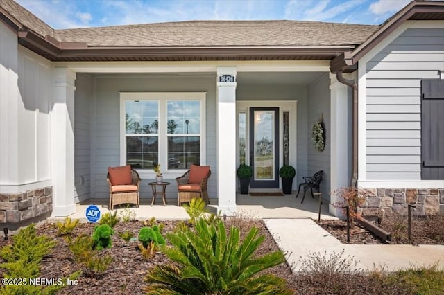 entrance to property with a porch, stone siding, and a shingled roof