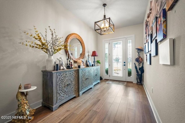 entrance foyer featuring baseboards, an inviting chandelier, wood finished floors, and a textured wall