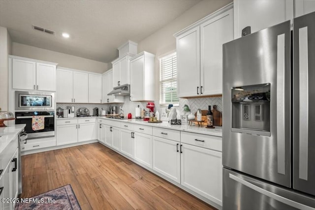 kitchen with visible vents, stainless steel appliances, light countertops, under cabinet range hood, and tasteful backsplash