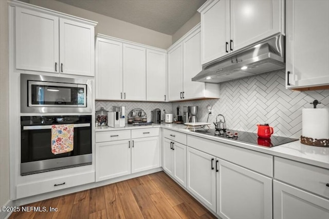 kitchen with under cabinet range hood, light wood-style flooring, white cabinetry, and stainless steel appliances