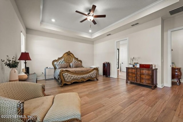 bedroom with visible vents, ornamental molding, a raised ceiling, and wood finished floors