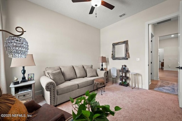 carpeted living area with visible vents, a textured ceiling, baseboards, and ceiling fan