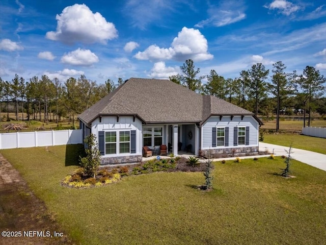 view of front of home with a front lawn, stone siding, fence, board and batten siding, and a shingled roof