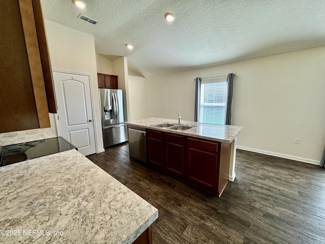 kitchen with an island with sink, dark wood-style flooring, a sink, stainless steel appliances, and light countertops