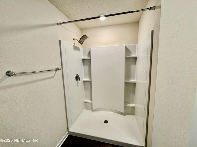 bathroom featuring a textured ceiling, a stall shower, and a textured wall