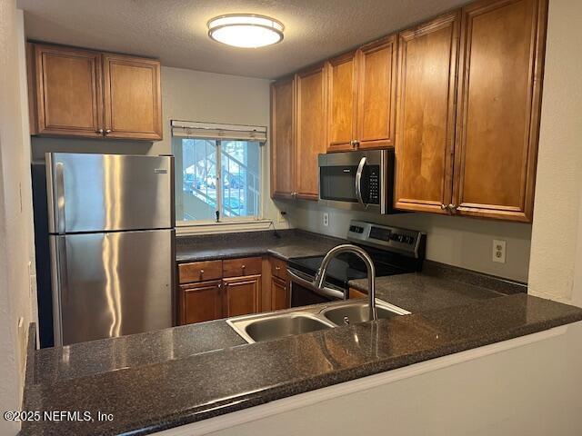 kitchen with dark stone counters, brown cabinets, appliances with stainless steel finishes, and a sink