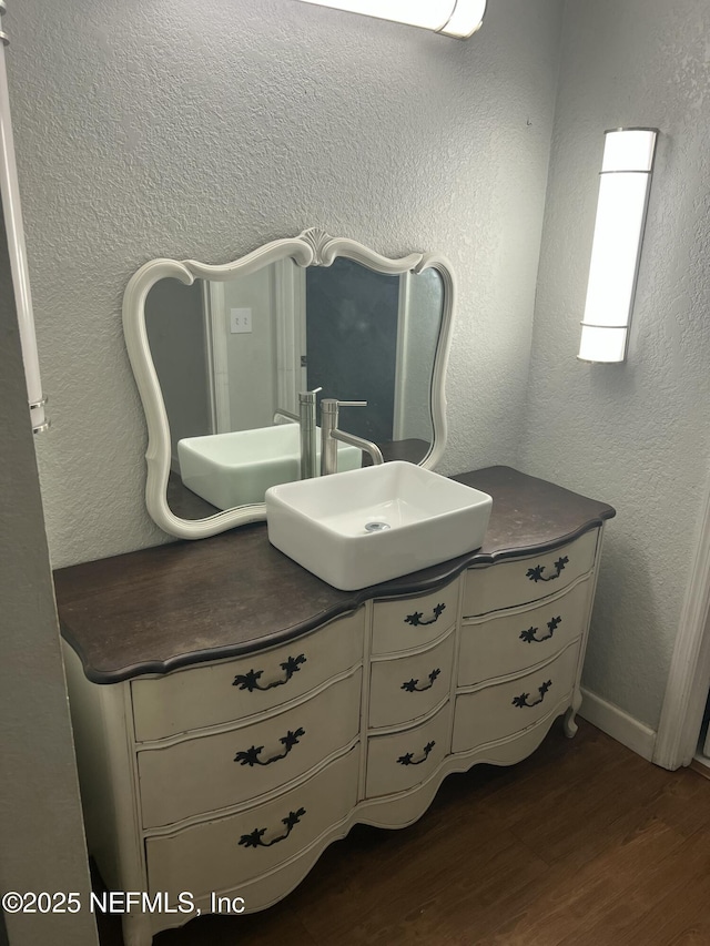 bathroom featuring a textured wall, vanity, baseboards, and wood finished floors