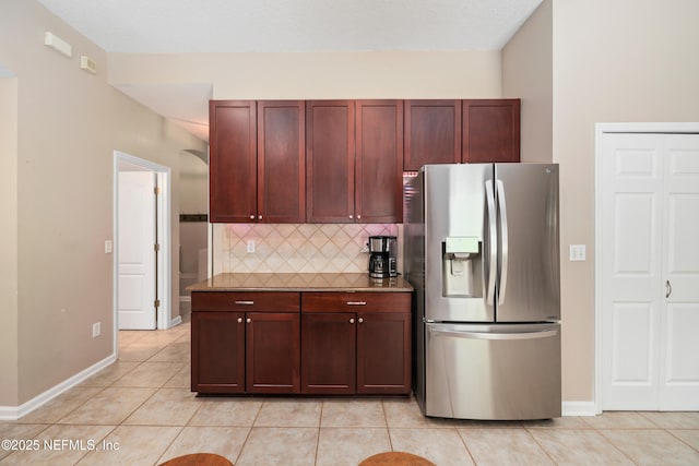 kitchen with light tile patterned flooring, stainless steel fridge with ice dispenser, baseboards, reddish brown cabinets, and backsplash